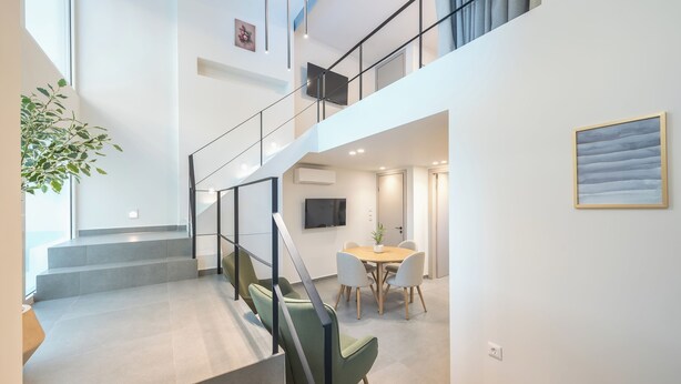 Un interior moderno con una escalera que lleva al segundo piso, un comedor con mesa y sillas, y un televisor de pantalla plana montado en la pared.