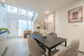 Een moderne eethoek met een donkere tafel, comfortabele stoelen, een vaas met bloemen, en een trap naar een hoger niveau.