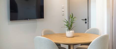 A conference room with a round wooden table, four grey chairs, a potted plant, and a flat-screen TV mounted on the wall.