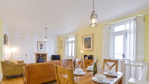 Ein Essbereich mit einem Holztisch, gedeckt für vier Personen, umgeben von Holzstühlen. Gegen die Wand lehnt ein Fernseher auf einem Schrank, und im Hintergrund ist ein Kamin zu sehen.
