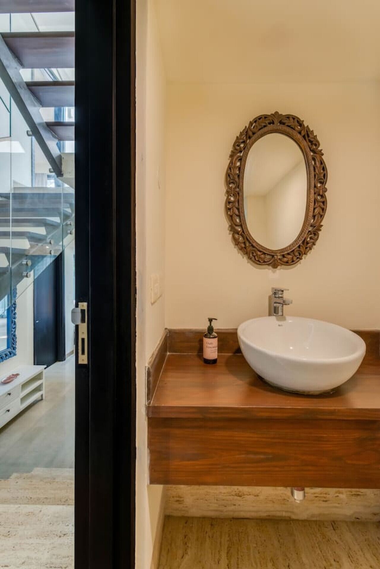 A bathroom with a white sink, a decorative mirror, and a bottle of lotion on the counter.