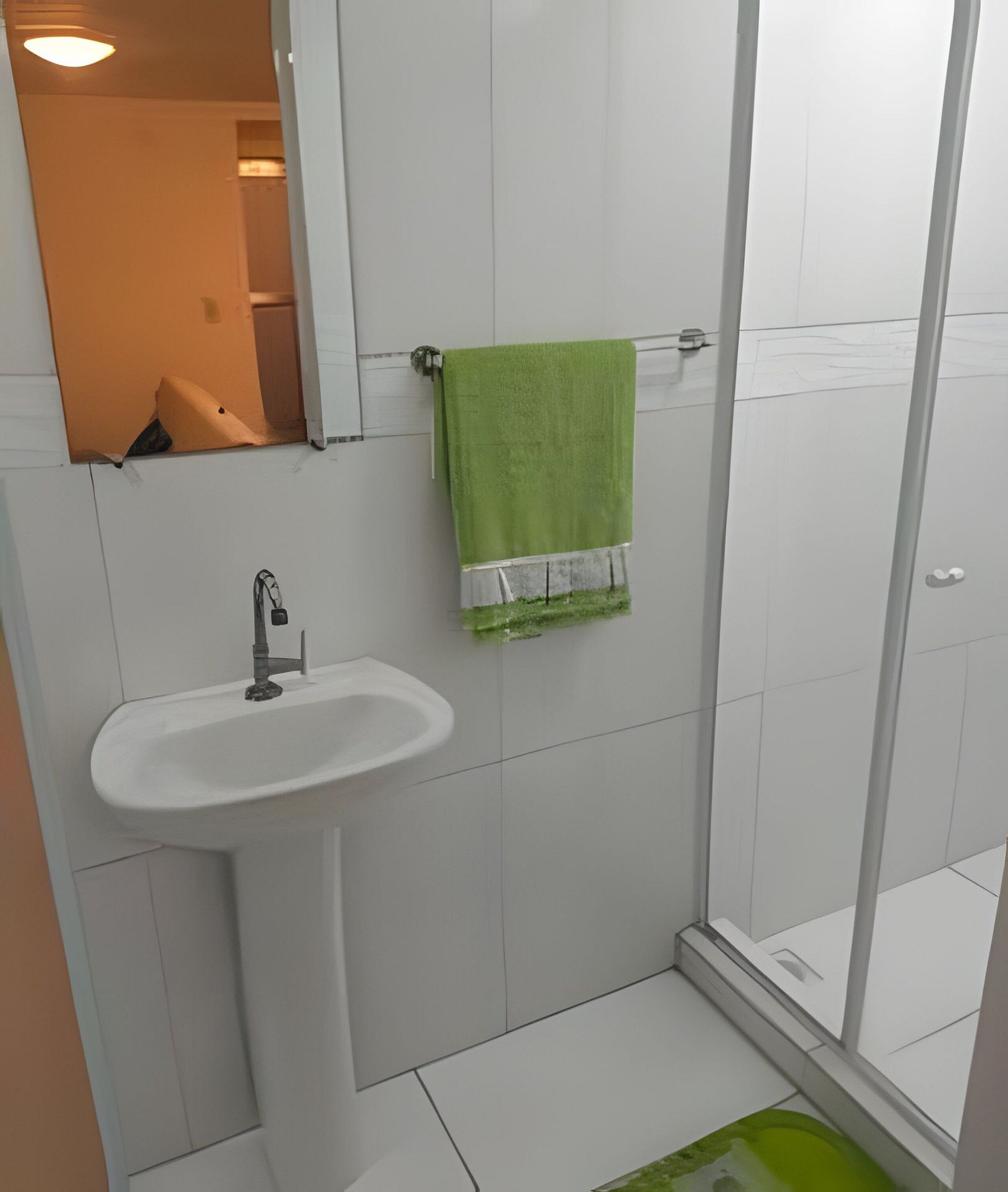 A bathroom with a white sink, a green towel, and a glass shower enclosure.