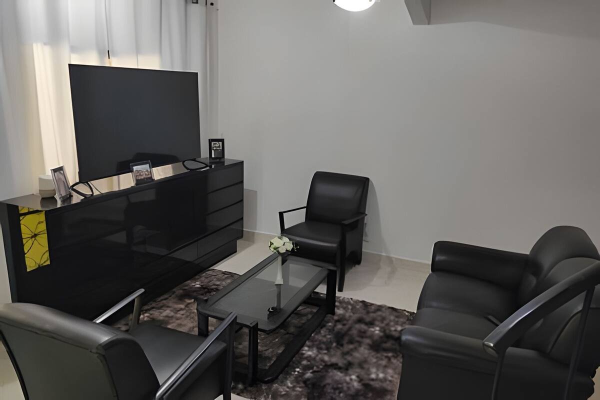 Un salon moderne avec un téléviseur à écran plat, un canapé en cuir noir, une table basse en verre et un meuble noir.