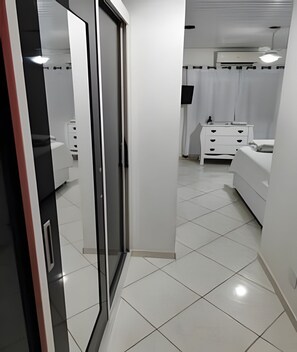 Een moderne slaapkamer met een glazen deur naar een badkamer, witte betegelde vloeren en een witte dressoir met lades.
