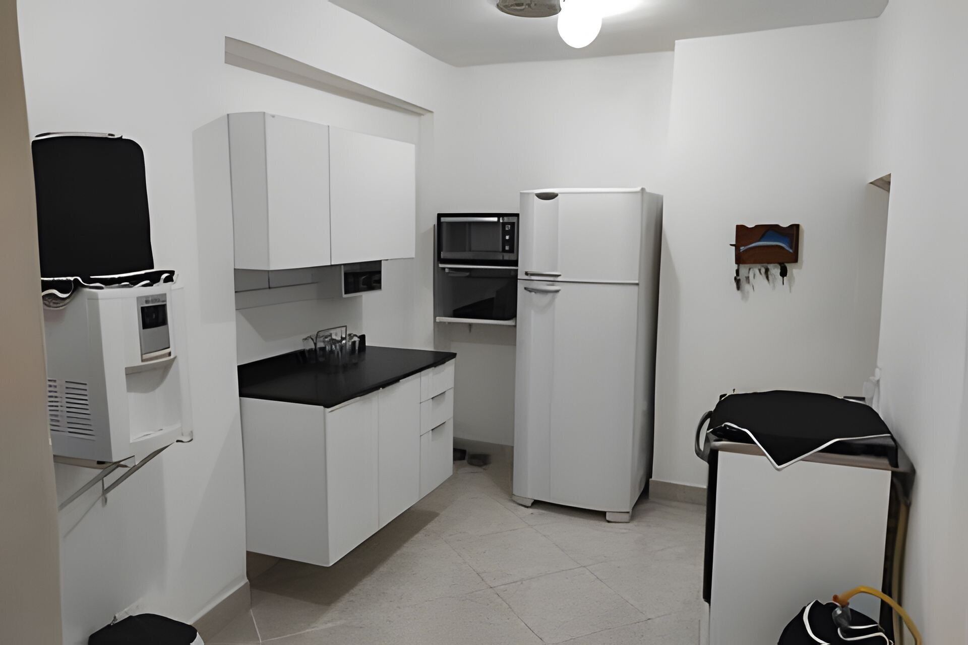 A compact kitchen with white cabinets, a black countertop, a microwave, and a refrigerator.