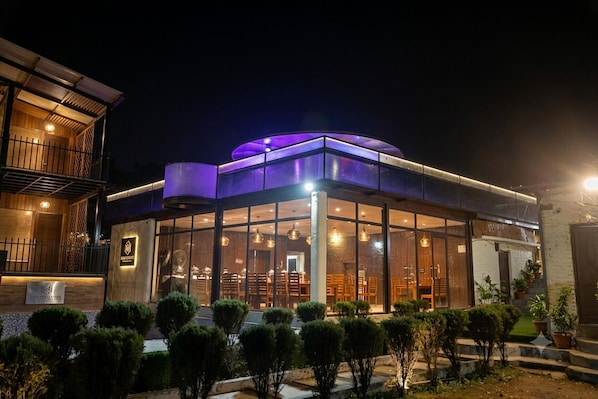 A modern building with a glass facade, a wooden deck, and a well-lit entrance. - Ambika Villa - A Unit Of D-Musk Hospitality (Rishikesh)