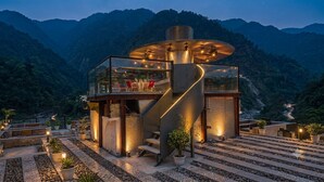 A modern building with a glass enclosure, a spiral staircase, and a view of a mountainous landscape. - Ambika Villa - A Unit Of D-Musk Hospitality (Rishikesh)