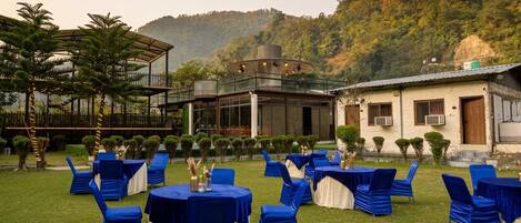 An outdoor seating area with tables and chairs, a covered structure, and a building with a white facade.