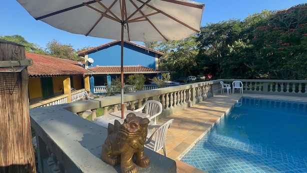 Un área de piscina con una estatua, una zona de estar cubierta y un edificio de fachada azul.