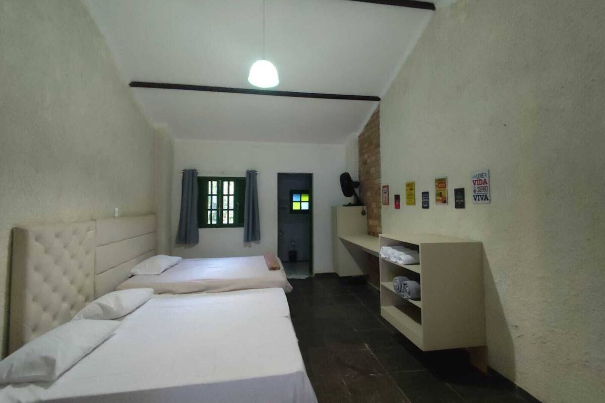 A room with two beds, a small desk, a brick wall, and a door leading to another room.