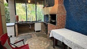 Una cocina con un horno de ladrillo, una ventana con vistas a la vegetación, una silla roja y una mesa con mantel blanco.
