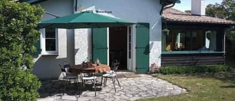 Een huis met een stenen terras, een eettafel en stoelen.