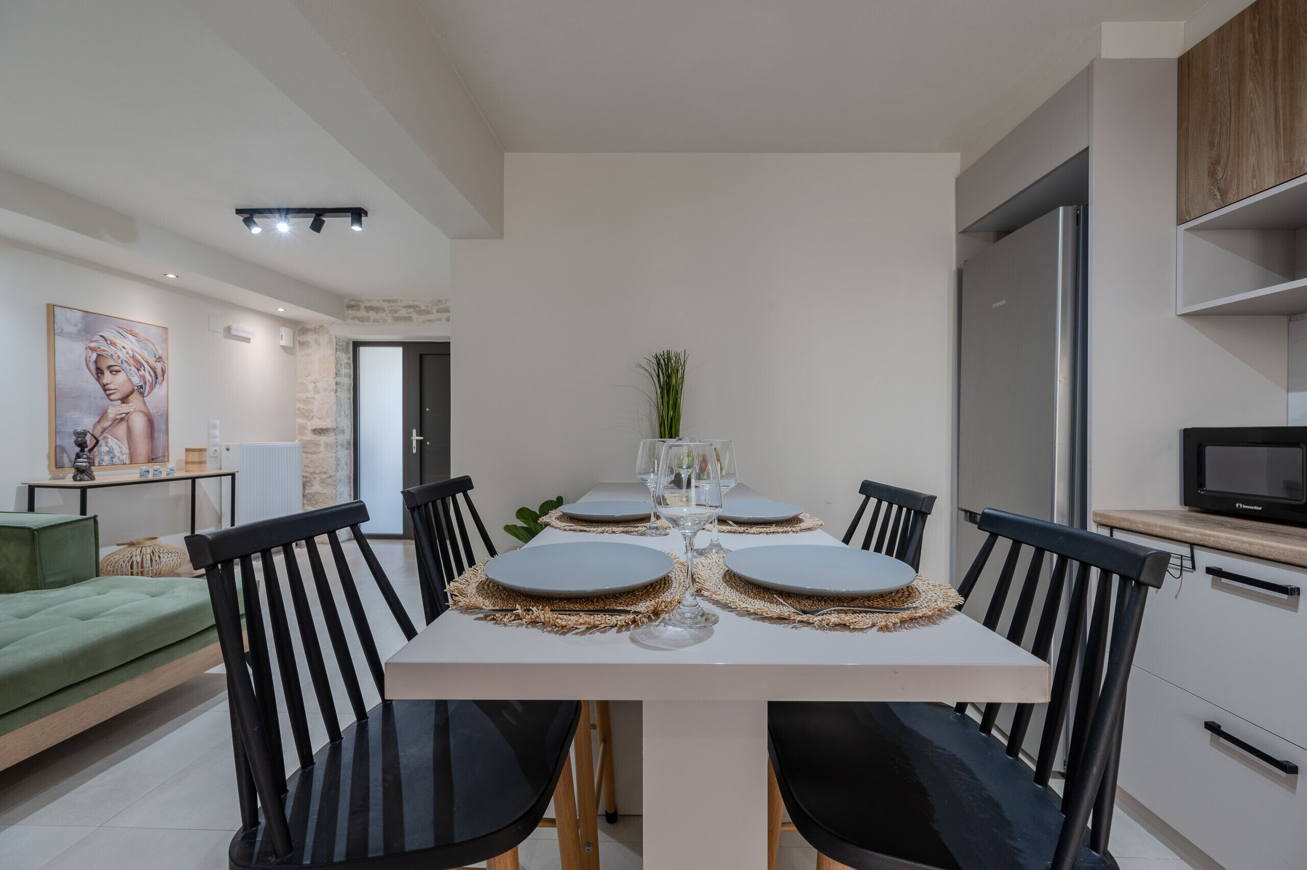 Un espace repas moderne avec une table blanche dressée pour quatre personnes, des chaises noires et un vase central.