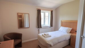 A hotel room with a single bed, a chair, a desk, a mirror, and a window with curtains. - Jubilee First-floor Single Bedroom (Penrith)