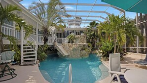 Une piscine intérieure agrémentée d’un élément rocheux, entourée de palmiers et de rampes blanches.