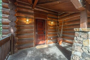 A log cabin with a wooden door, two wall-mounted lanterns, a stone wall, and a wooden floor. - Summit Cabin 3 Bedroom Home (Telluride)