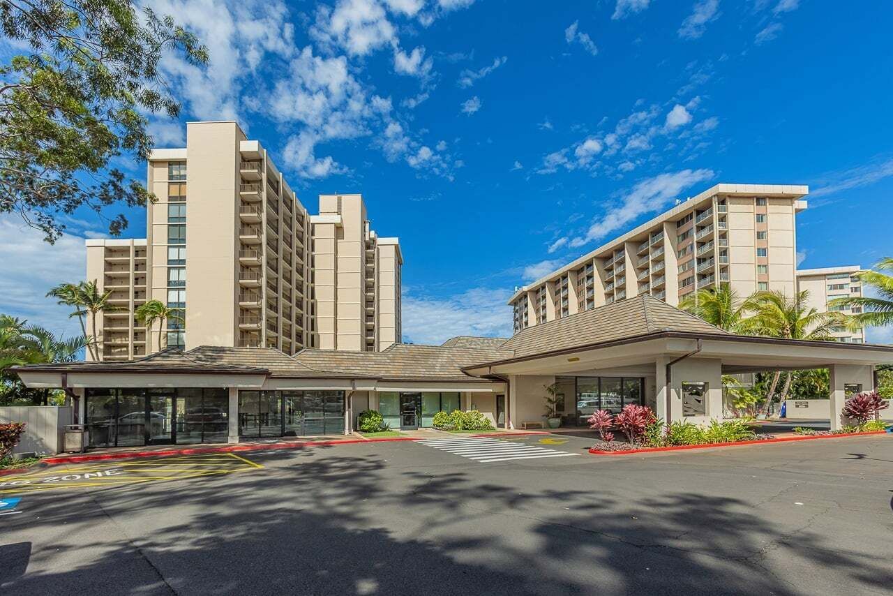 A hotel with a modern architectural design, featuring a central building with multiple floors and a flat roof, surrounded by a landscaped area with palm trees.