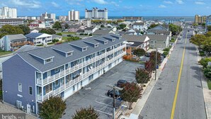 Een meerlaags hotel met een parkeerplaats, een weg met een dubbele gele lijn, en een uitzicht op de oceaan en andere gebouwen op de achtergrond.