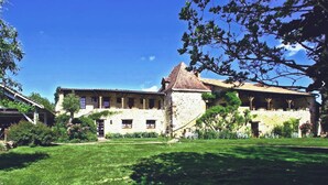 Ein traditionelles Steinhaus mit Ziegeldach, umgeben von einem gepflegten Rasen und Bäumen.