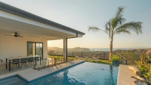 Ein Pool mit Bergblick, eine überdachte Terrasse mit Stühlen und eine Palme.
