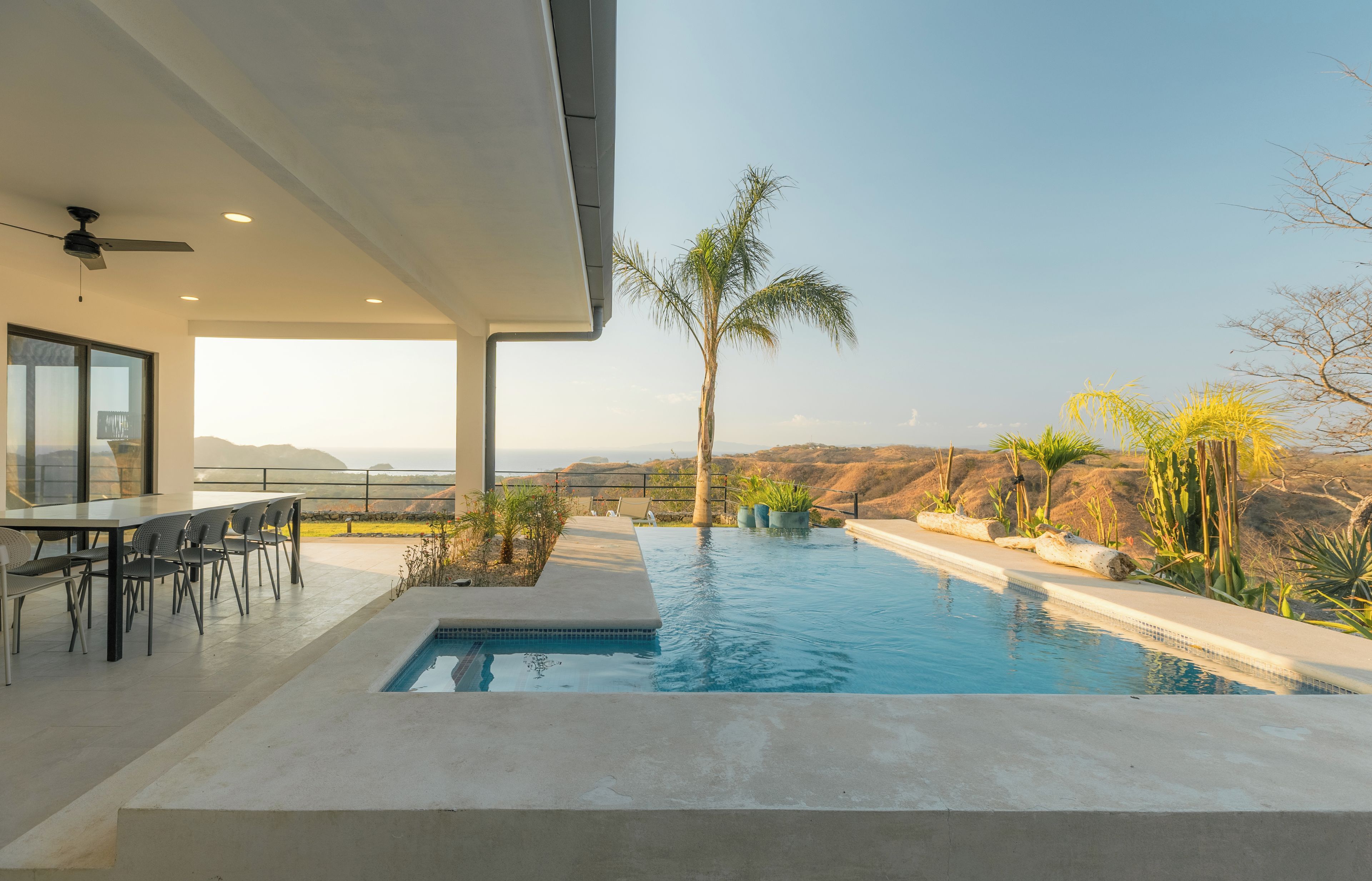 A modern outdoor pool area with a dining setup and a view of the hills.