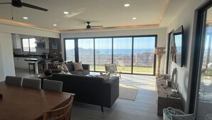 Ein großzügiger Wohnbereich mit Esstisch, Sofas und einer großen Schiebeglastür, die auf einen Balkon mit Blick auf die Berge führt.