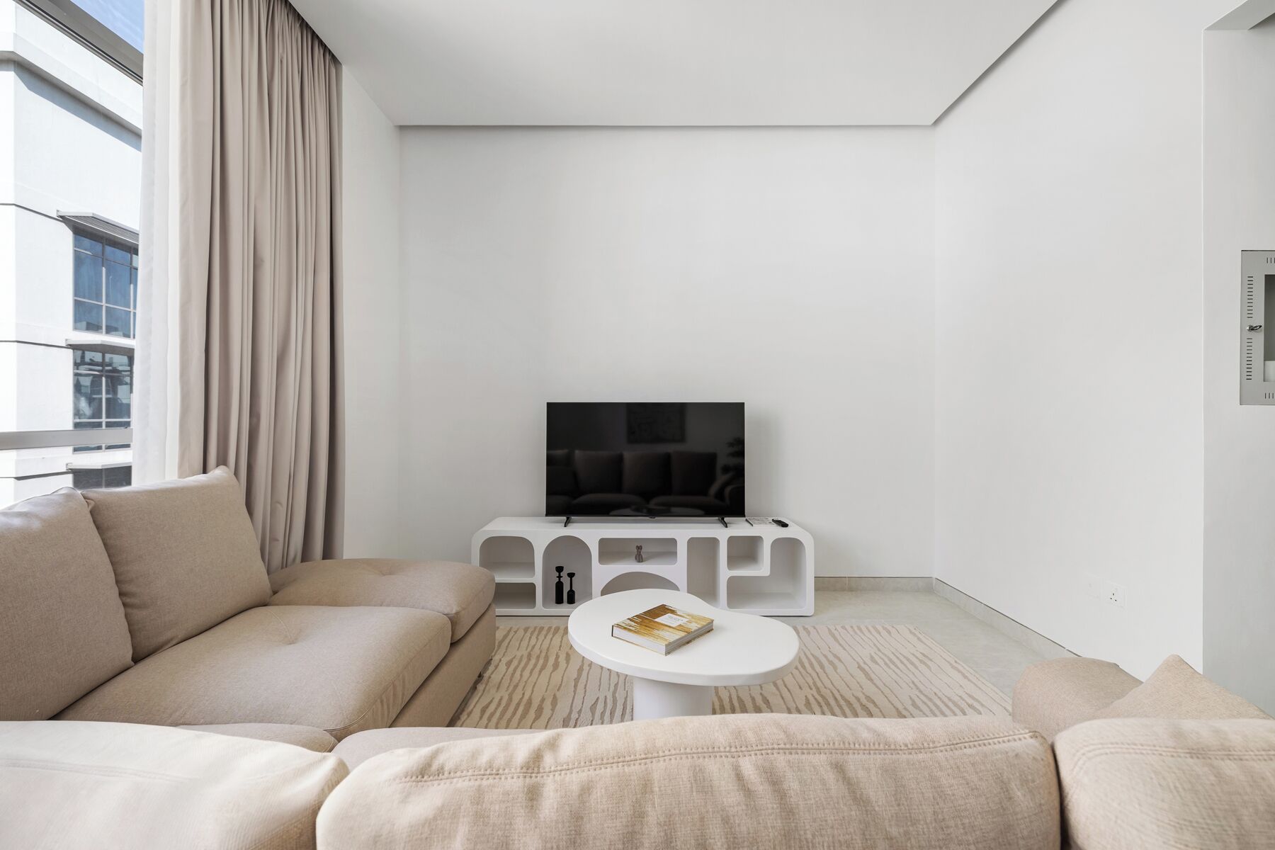 Un soggiorno moderno con un divano, un tavolino da caffè e una TV su un mobile bianco.