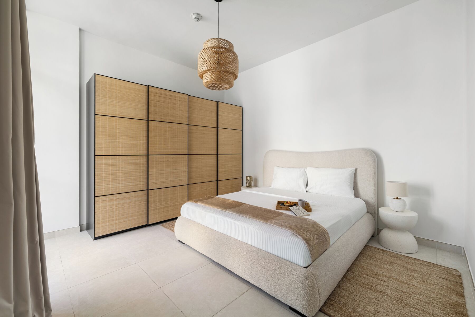 A modern bedroom with a large bed, a wooden wardrobe, a hanging light fixture, and a bedside table with a lamp.