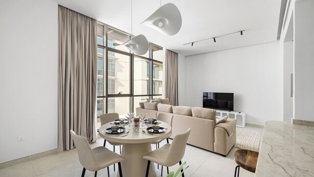 Ein modernes Wohnzimmer mit einem runden Esstisch, einem beigen Sofa und einem Flachbildfernseher.