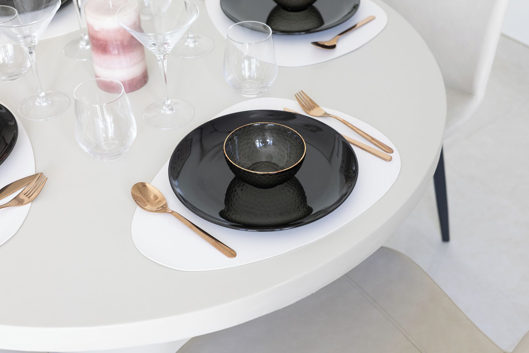 A round dining table with black plates, gold cutlery, and clear glasses.