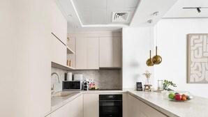 Eine moderne Küche mit hellen Schränken, einer Marmorarbeitsplatte, einem eingebauten Ofen und einem kleinen Essbereich mit einer Obstschale.