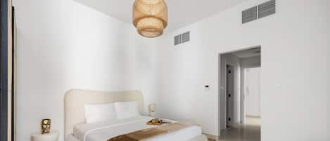 A modern bedroom with a large bed, a bedside table, a lamp, and a hanging light fixture.