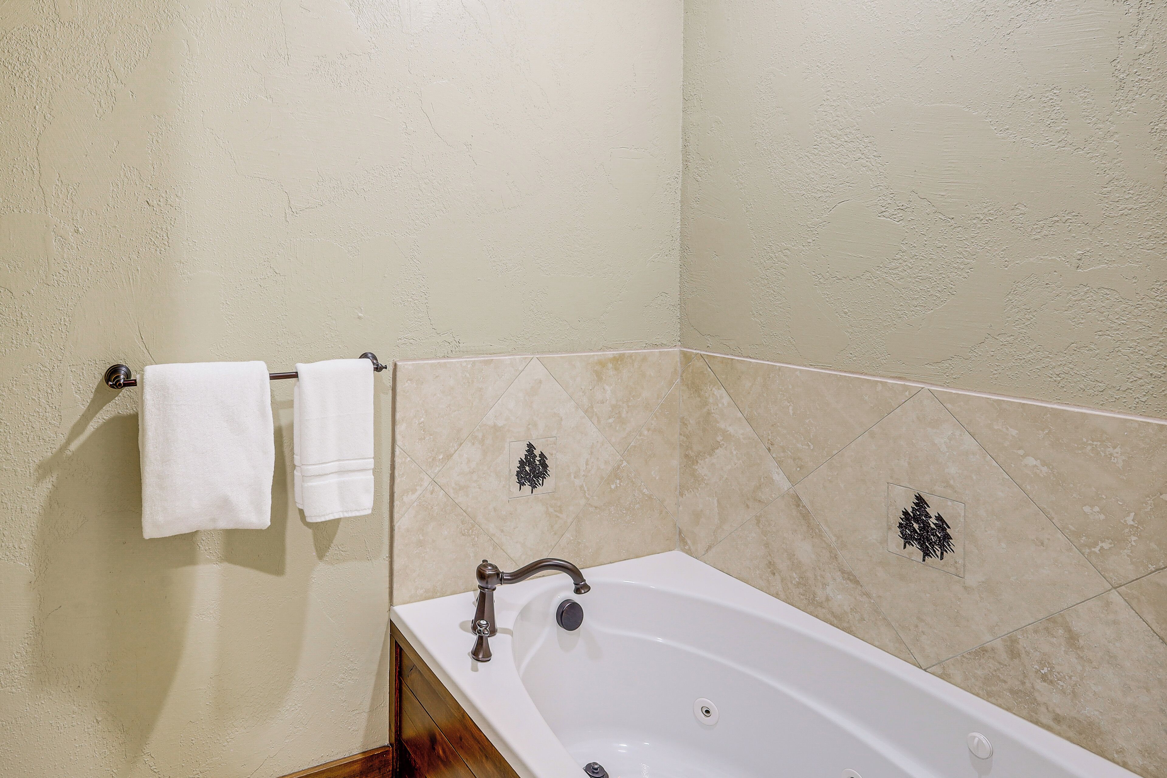 A bathroom with a bathtub, two white towels hanging on a towel rack, and decorative tiles on the wall.