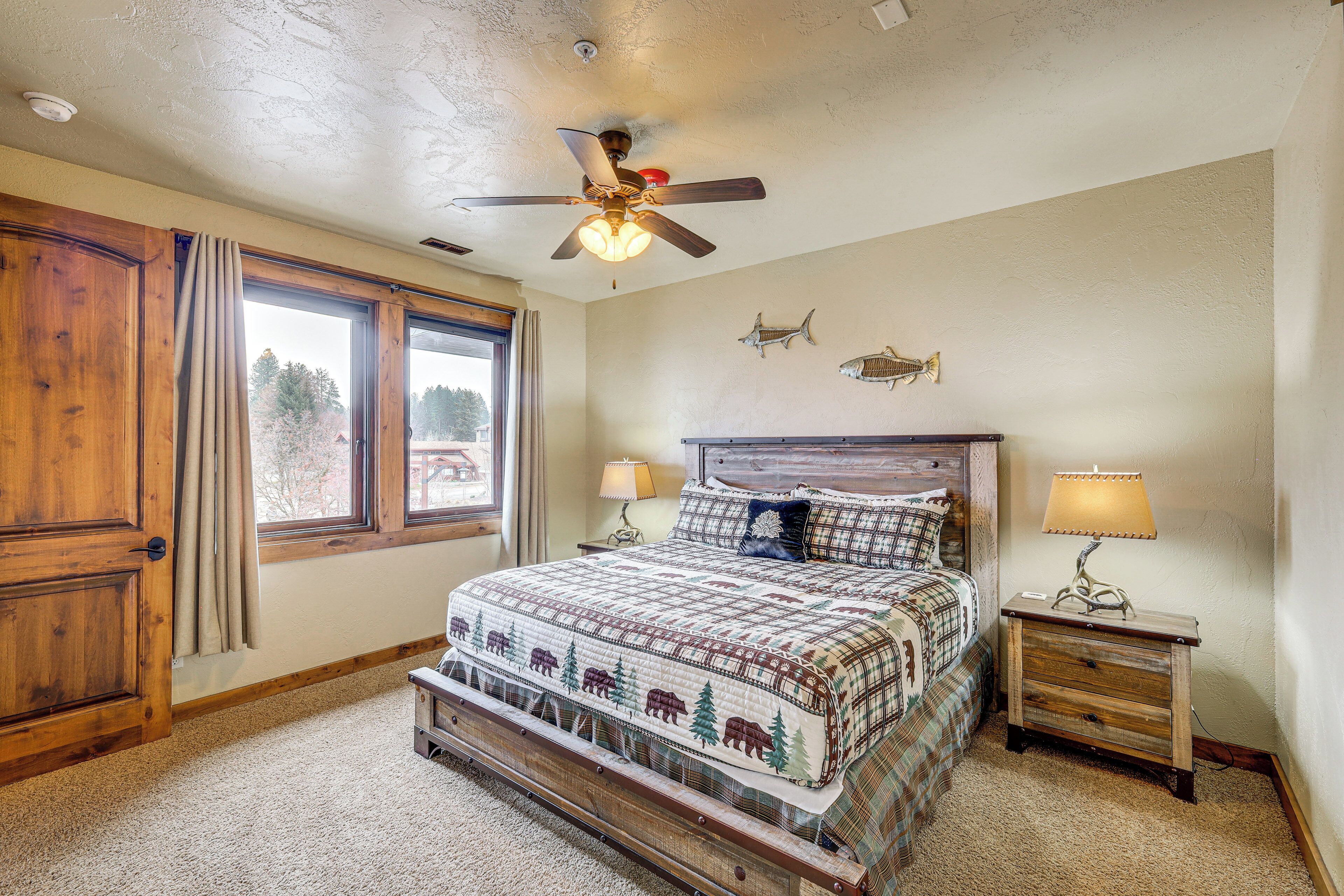 A bedroom with a bed, wooden headboard, two bedside tables with lamps, a ceiling fan, and a window with curtains.