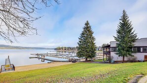 Une propriété au bord du lac, dotée d’un quai, d’un grand arbre à feuilles persistantes et d’un bâtiment avec un balcon.