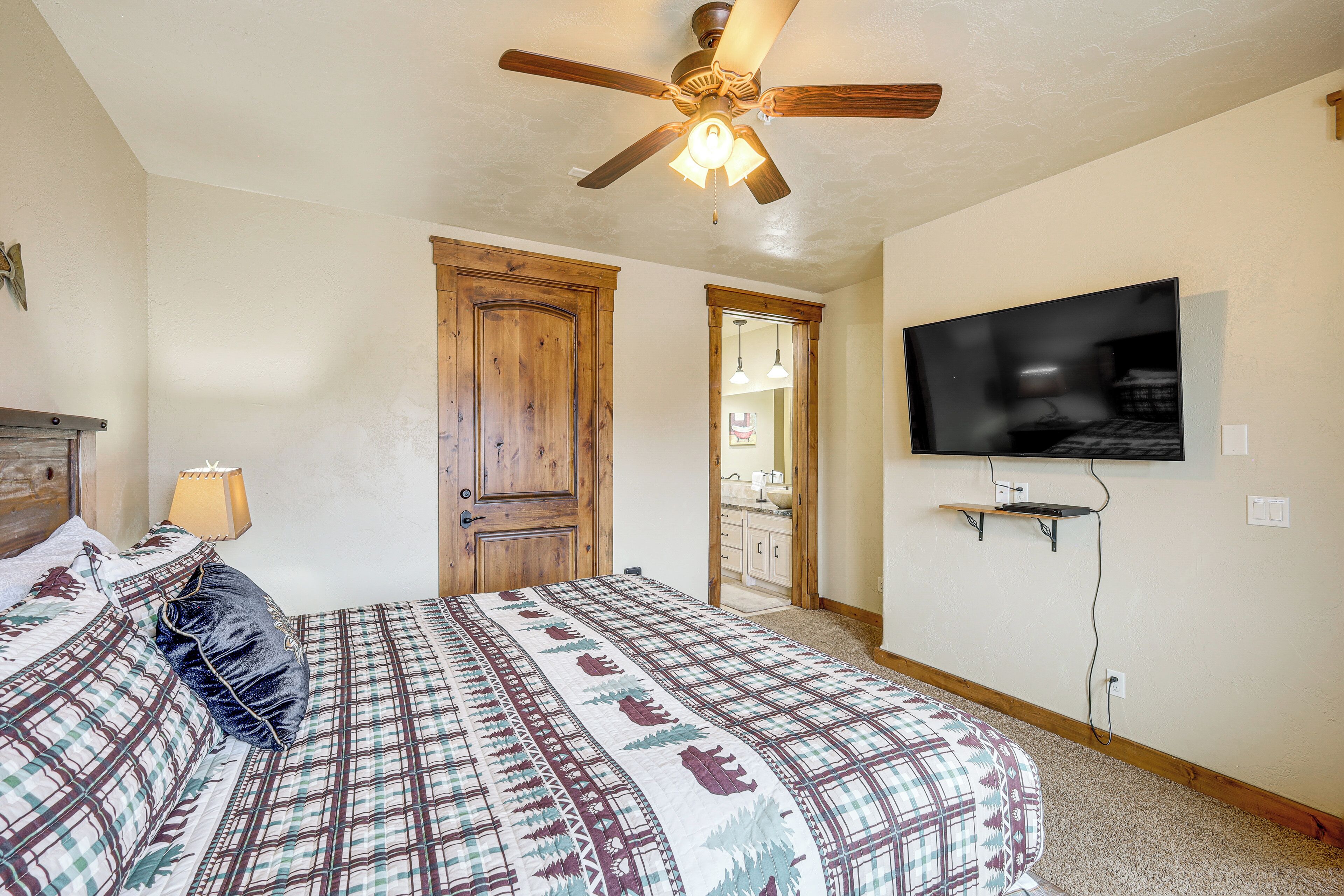 Ein Schlafzimmer mit einem Bett, einem Deckenventilator, einem an der Wand befestigten Fernseher und einer Holztür.
