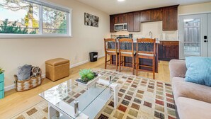 Una sala de estar moderna con una mesa de centro de vidrio, un sofá color beige y una alfombra estampada.