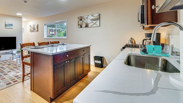 Una cocina moderna con una isla grande, armarios de madera, un lavamanos de acero inoxidable y una ventana que proporciona luz natural.