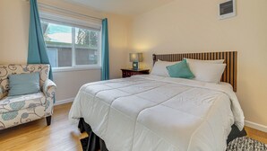 Un dormitorio con cama, una silla, una mesita de noche y una ventana con cortinas.