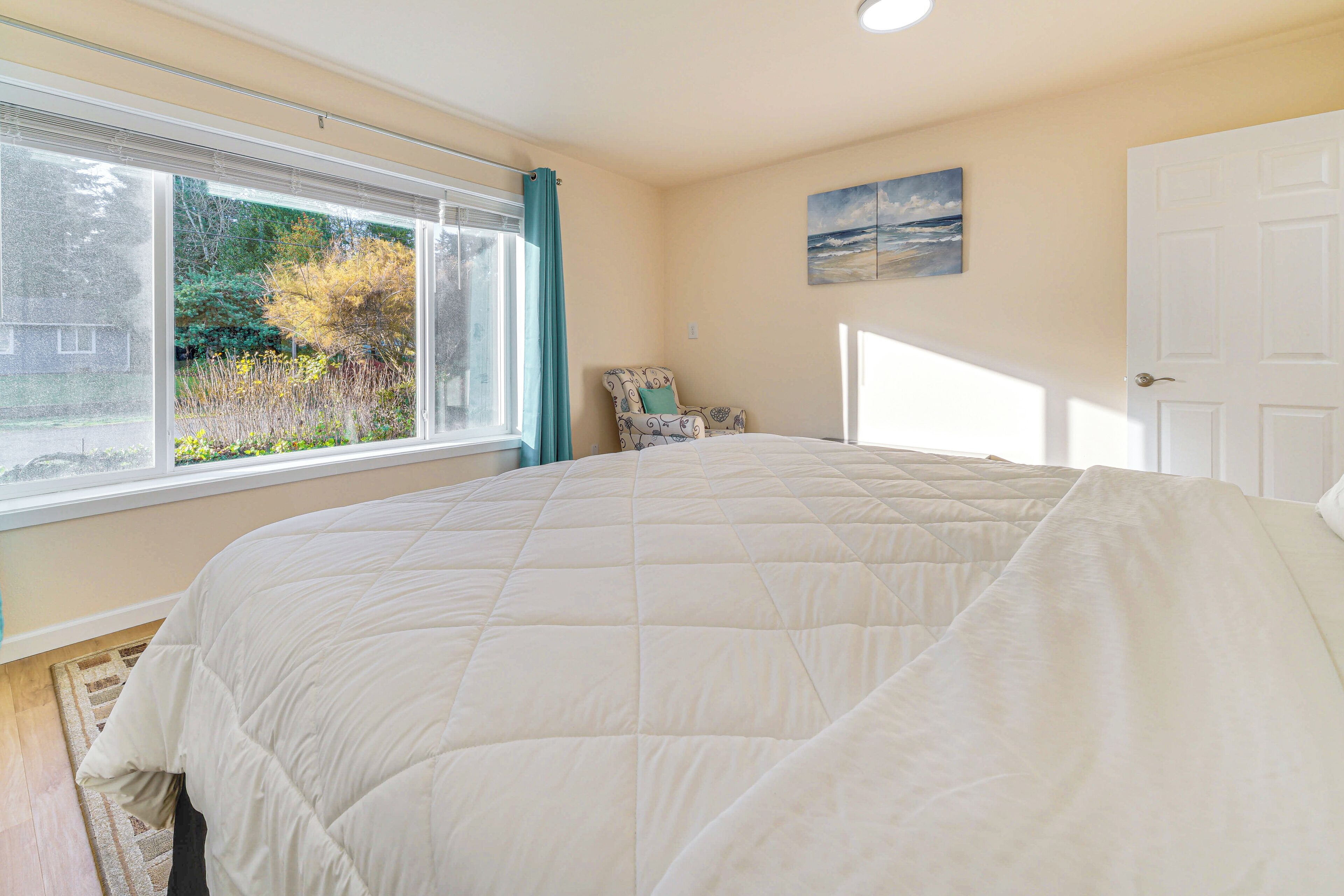 A bedroom with a large bed, a window with curtains, a chair, and a door.