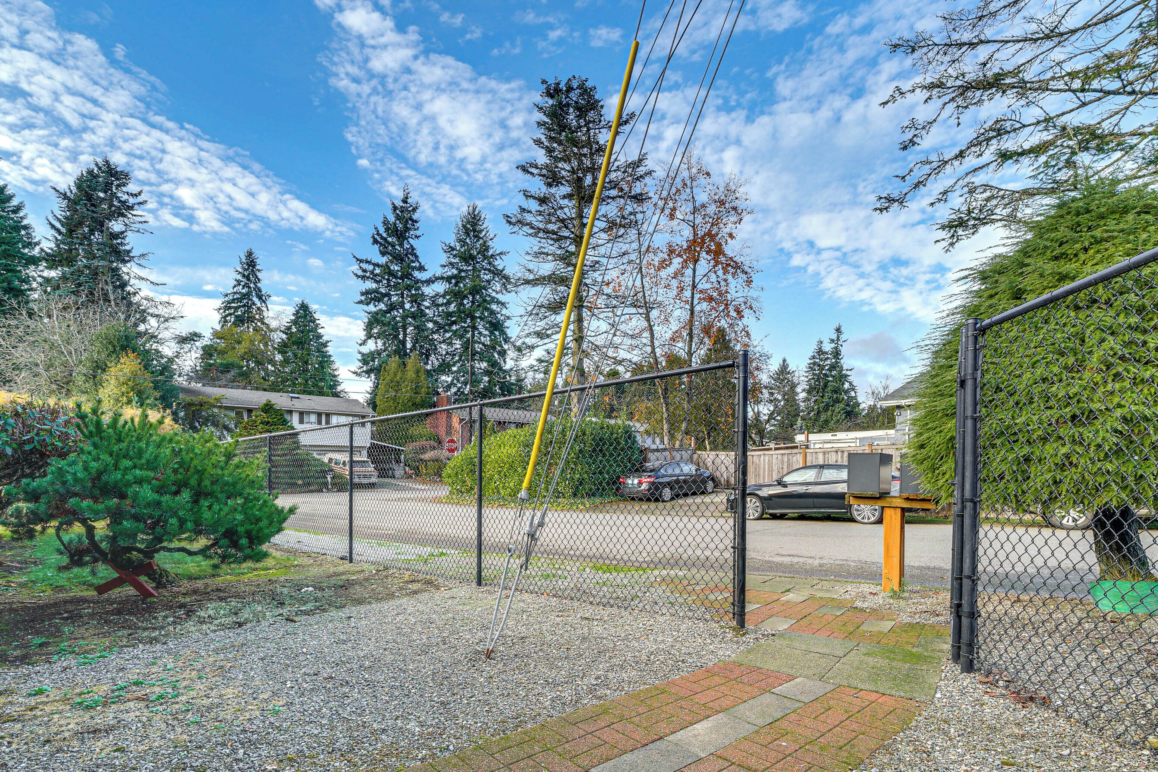 A fenced outdoor area with a gravel path, trees, and a parked car.