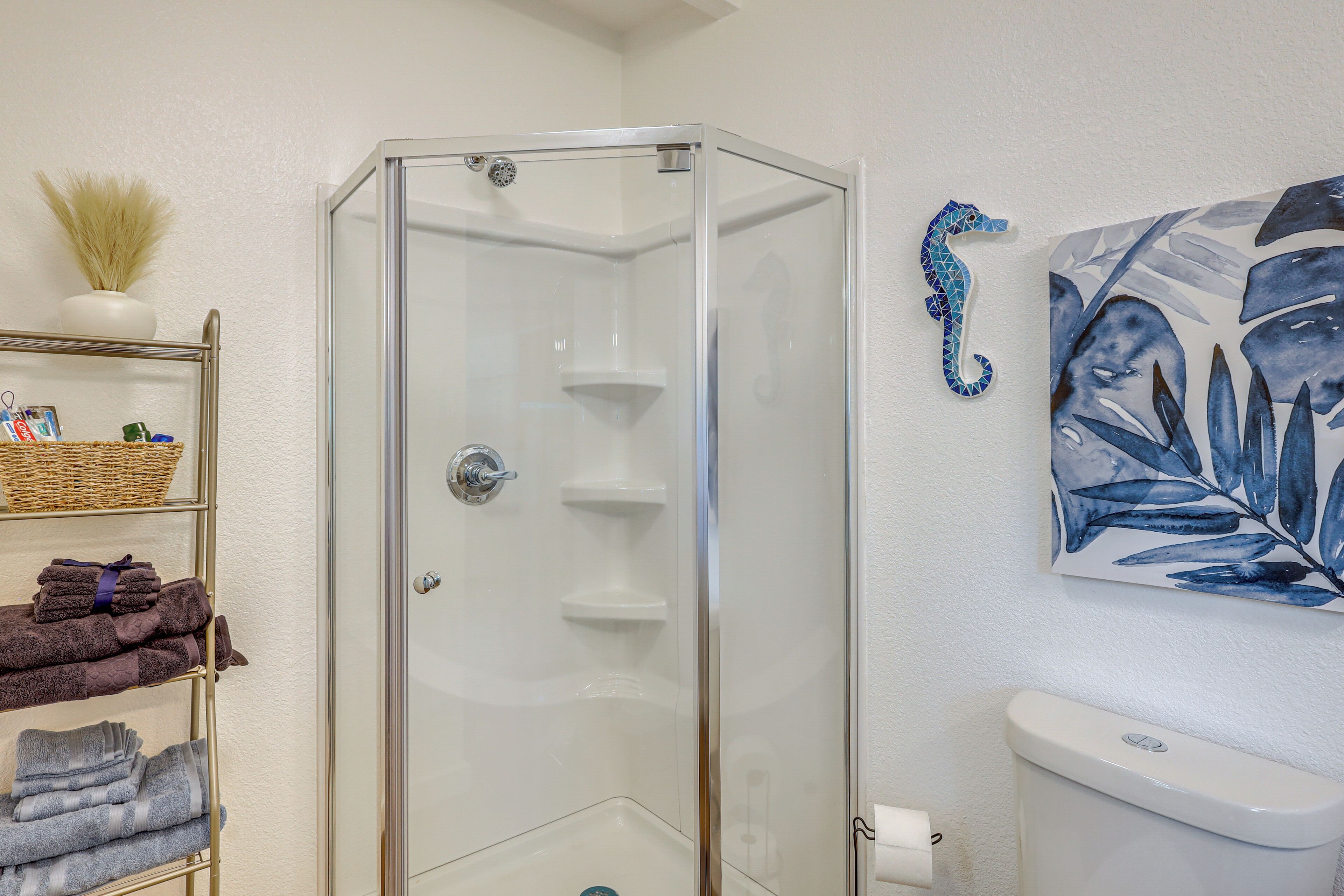 Un bany amb una cabina de dutxa de vidre, un vàter, una barra de tovalloles amb tovalloles doblegades i un cavallet de mar decoratiu a la paret.
