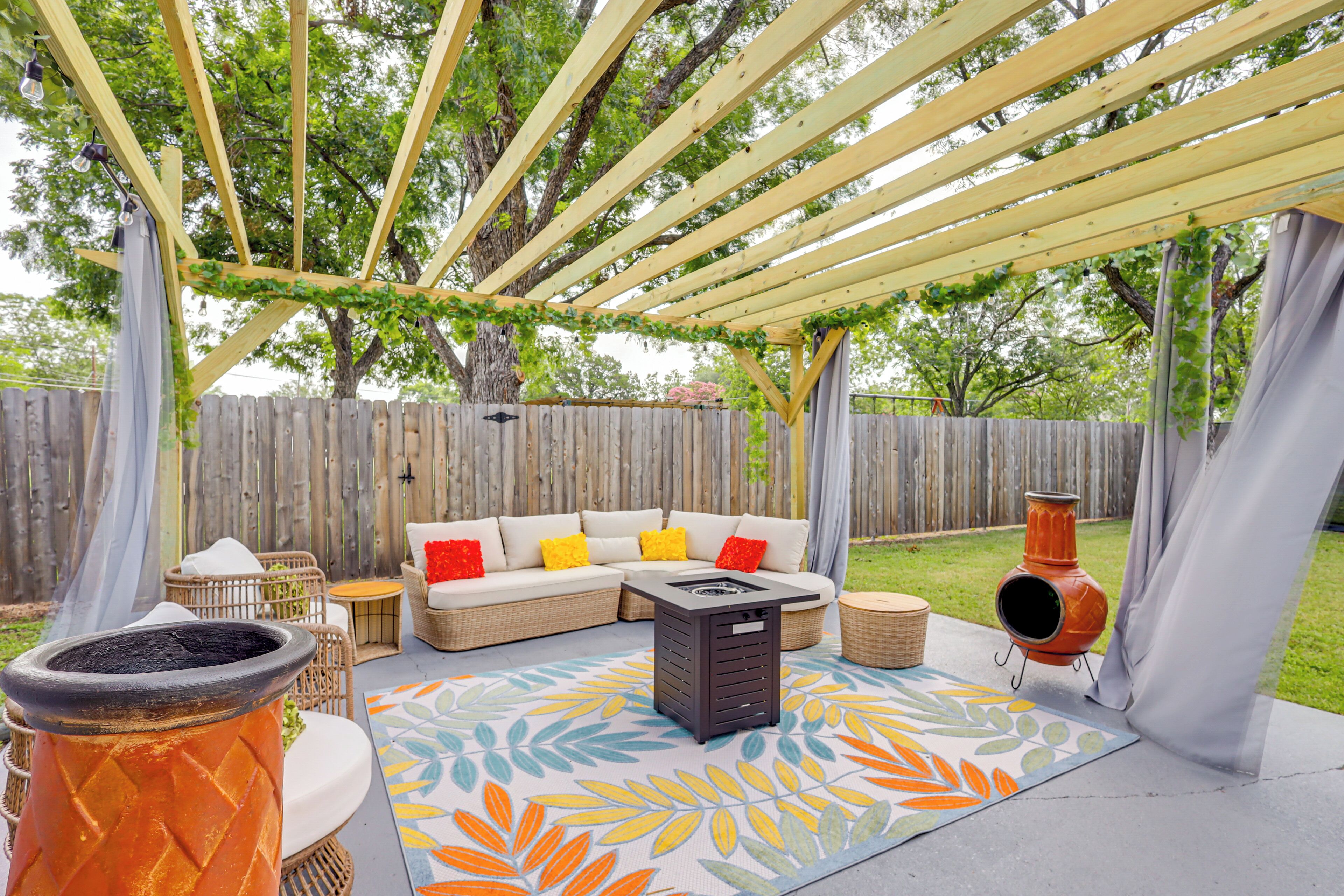 Un patio al aire libre con una pérgola de madera, un conjunto de sofás, un hogar para fuego y un tapete decorativo.