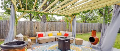Un patio al aire libre con una pérgola de madera, un conjunto de sofás, un hogar para fuego y un tapete decorativo.