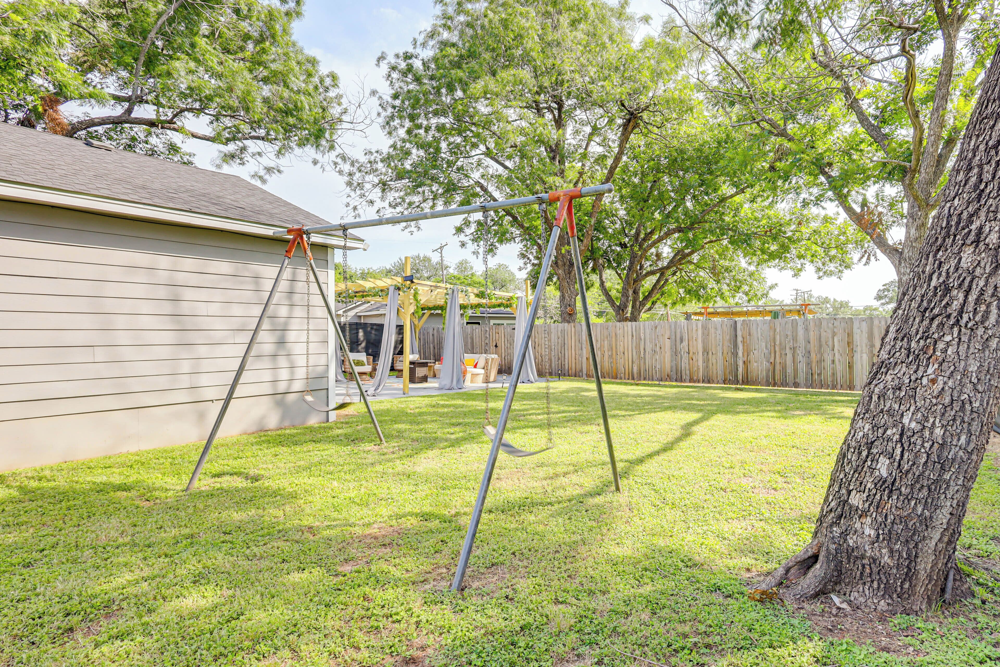 A backyard with a swing set, a wooden fence, and a tree.