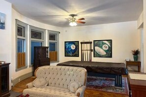 Une pièce dotée d’un ventilateur de plafond, d’une grande fenêtre, d’un canapé et d’œuvres d’art accrochées au mur.
