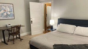 Een slaapkamer met een bed, een bureau, een stoel, een bedlampje en een deur.