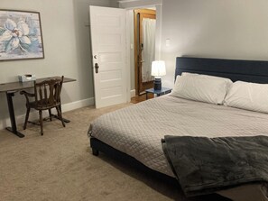 A bedroom with a bed, a desk, a chair, a bedside lamp, and a door. - NH2: Spacious 2BR Apt (DuBois)
