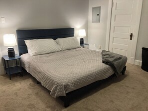 Una cama bien hecha con colcha acolchada, dos mesitas de noche con lámparas y una puerta con un pequeño ventanal.