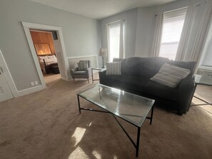 A living room with a glass coffee table, a dark sofa, a chair, and a lamp.